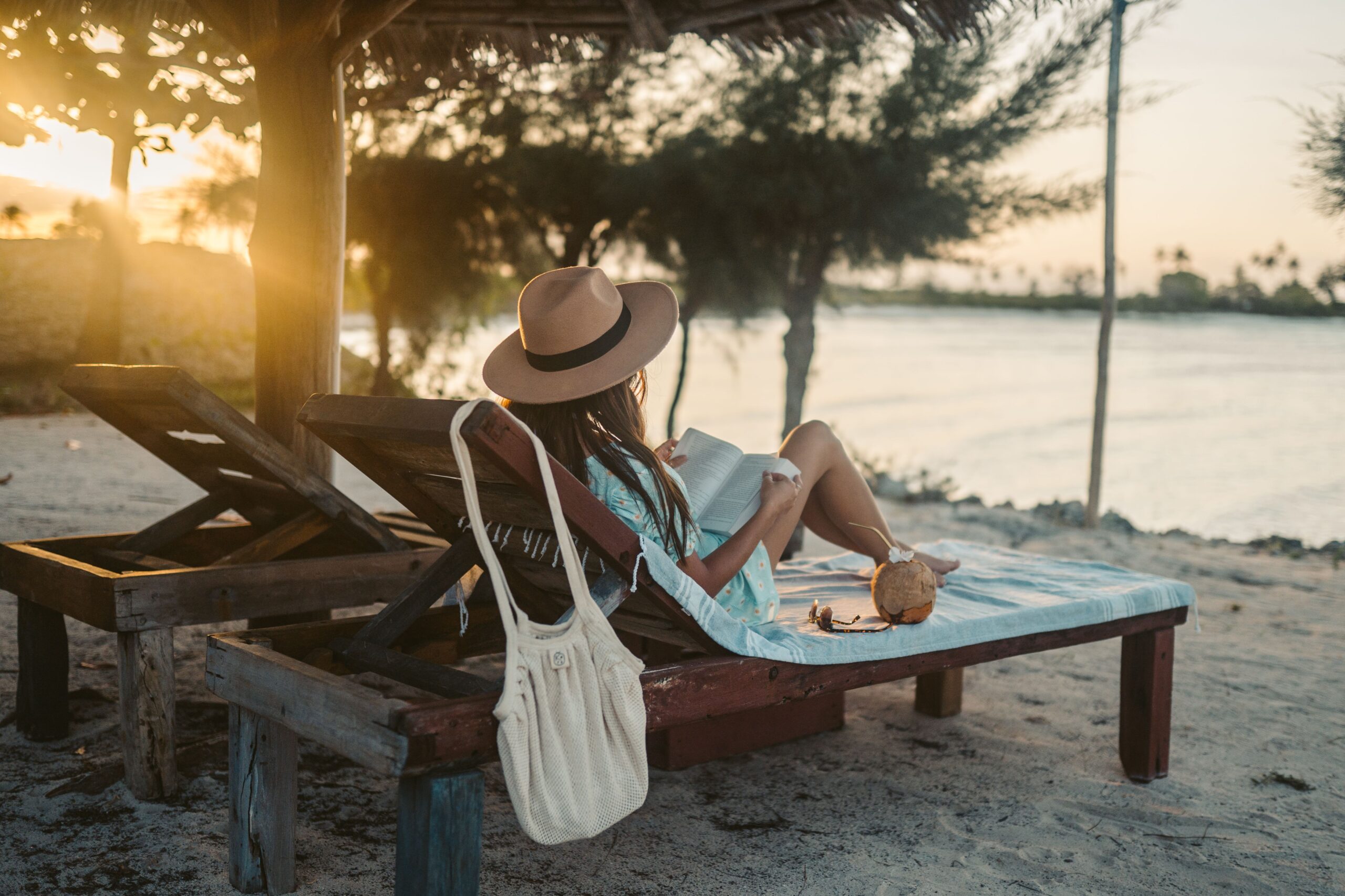 Home Woman reading on a beach lounger under a sun hat in Zanzibar at sunset, embracing vacation tranquility.